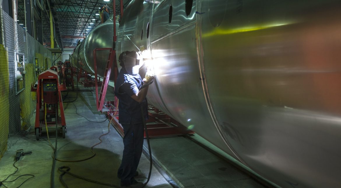 Worker welding large tank in factory